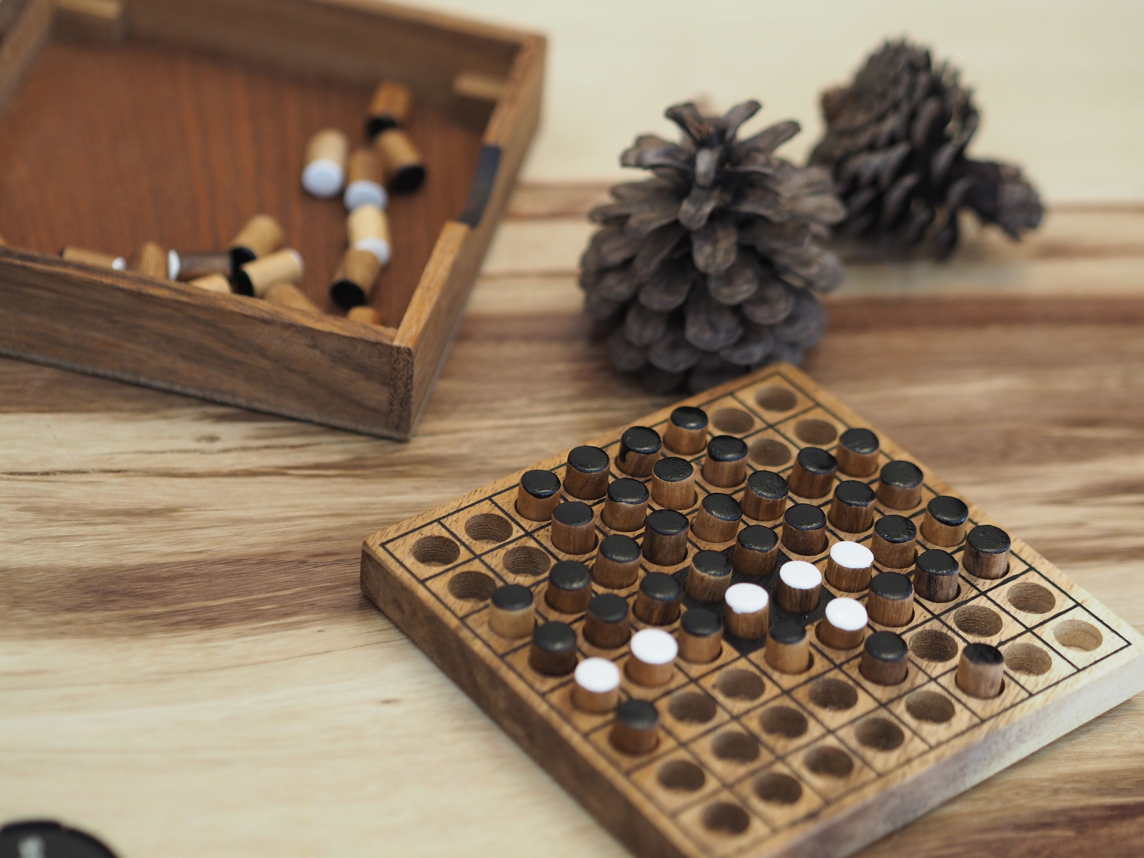 A wooden board game with a grid layout and cylindrical pieces, placed on a wooden surface.