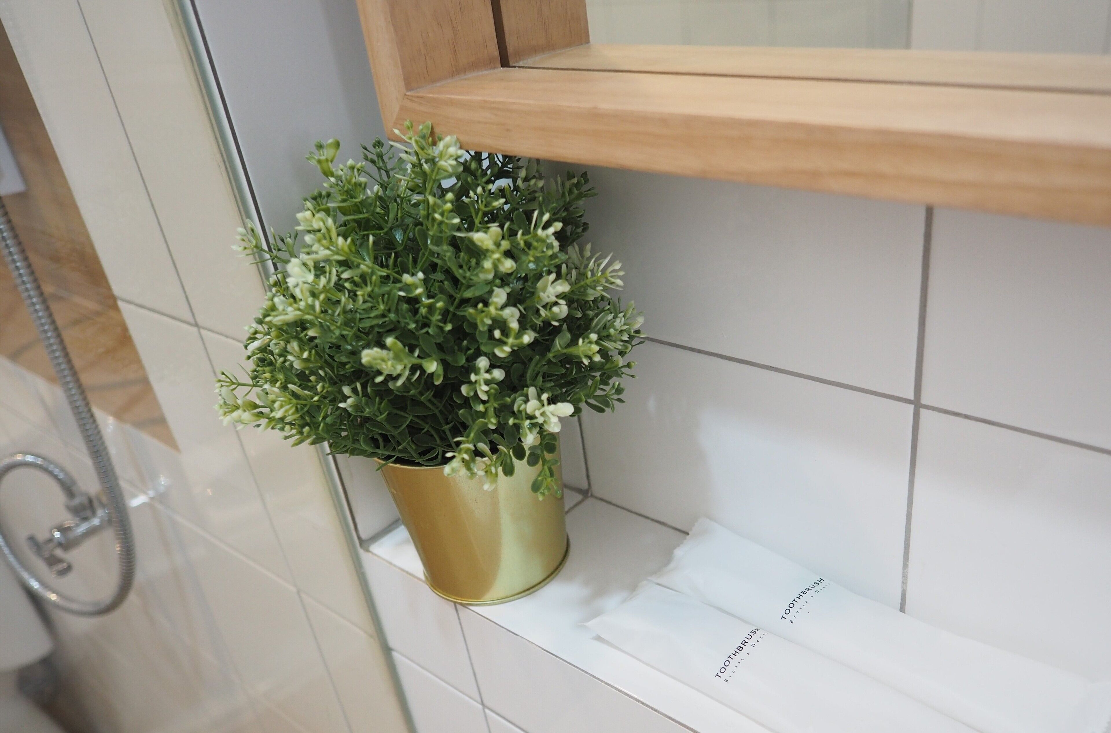 A bathroom with a potted plant on a shelf, a shower area, and a white tiled wall.