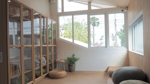 A room with a wooden floor, a glass cabinet with books, a plant, and two round ottomans. - Nornnuea at Inthanon (Chom Thong)