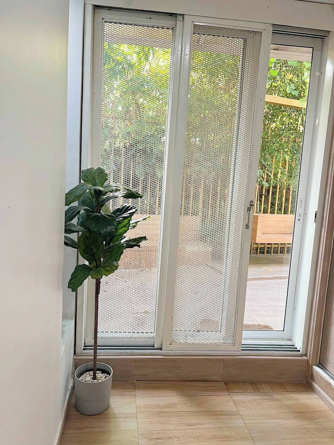 A sliding glass door with a mesh screen, a potted plant, and a view of a wooden deck and greenery outside.