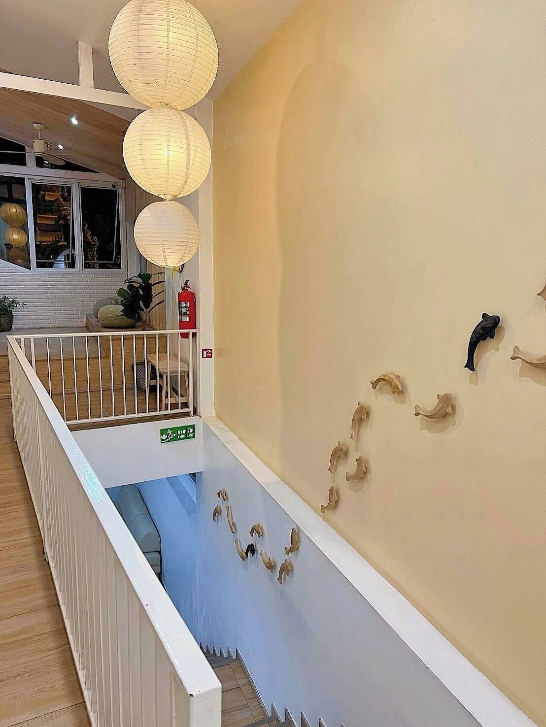 A staircase with a white railing, a beige wall with decorative wall art, and hanging paper lanterns.