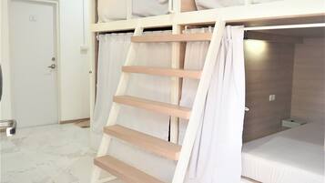 Dormitorio con literas, una escalera de madera, cortinas blancas y una puerta blanca.