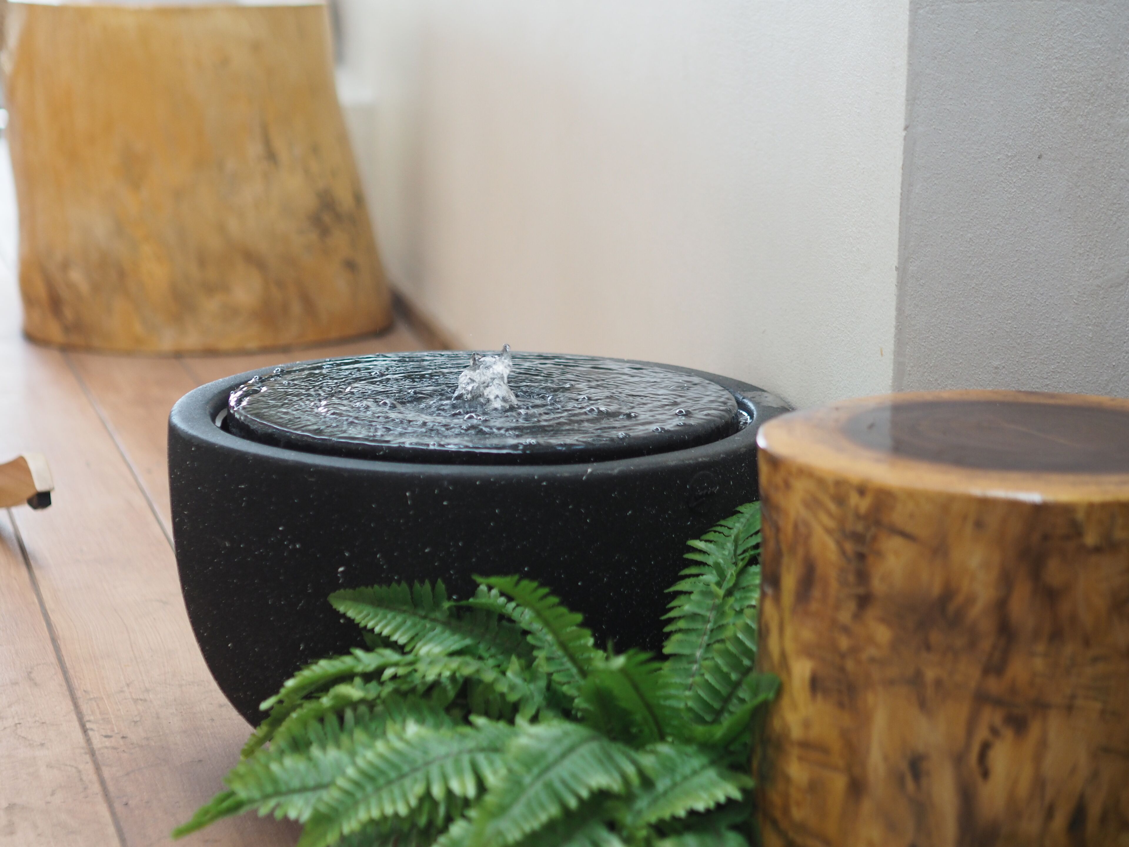 A black water feature with a wooden base and a wooden stool nearby.