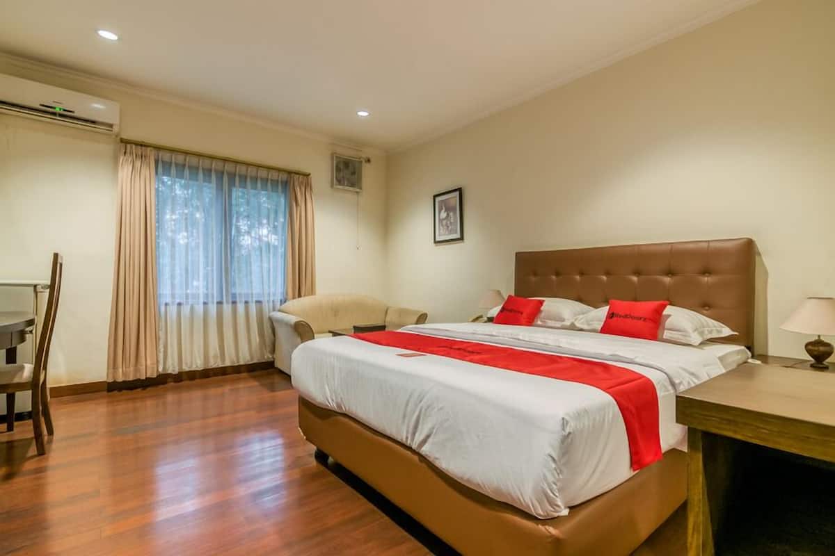 Habitació d'hotel amb un llit gran, una taula, una cadira i una finestra amb cortines.