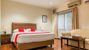 A hotel room with a large bed, a bedside table, a chair, and an air conditioning unit. - Reddoorz Plus Near Dharmawangsa Square (Jakarta)