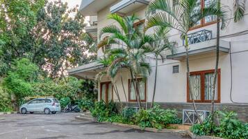 A multi-story building with balconies, surrounded by lush greenery and a parked car.