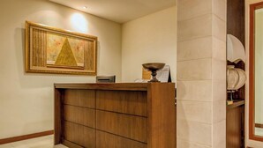 A reception desk with a wooden finish, a framed artwork above it, and a wall-mounted calendar. - Reddoorz Plus Near Dharmawangsa Square (Jakarta)