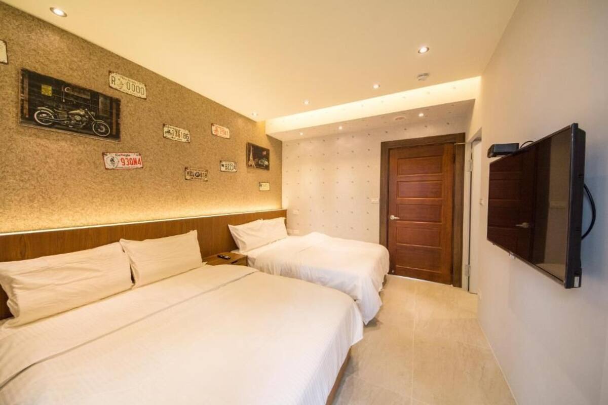 Een hotelkamer met twee bedden, een tv aan de muur en een wand versierd met oude kentekenplaten.