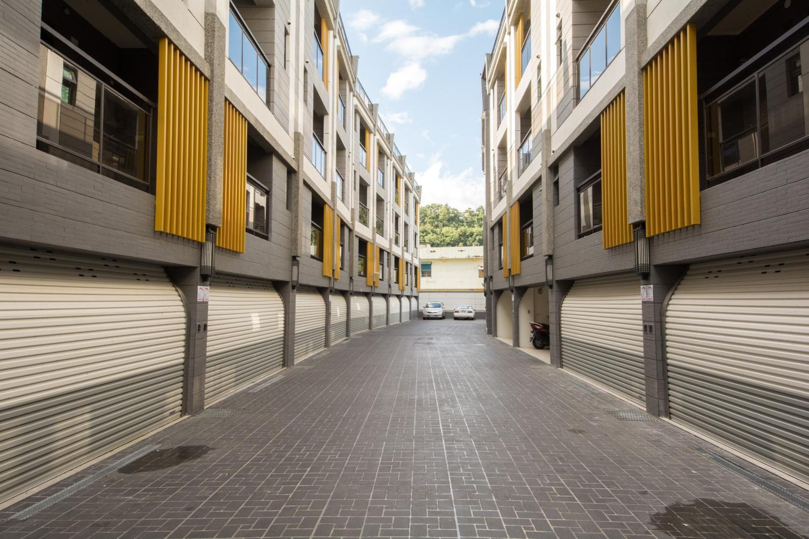 En lång, överbyggd korridor med stängda garageportar, som leder fram till en byggnad med många fönster och gula, vertikala detaljer.