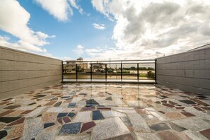 Ein geräumiger Balkon mit Mosaikboden und Glastrennwand, der Blick auf Gebäude und Grünflächen bietet.