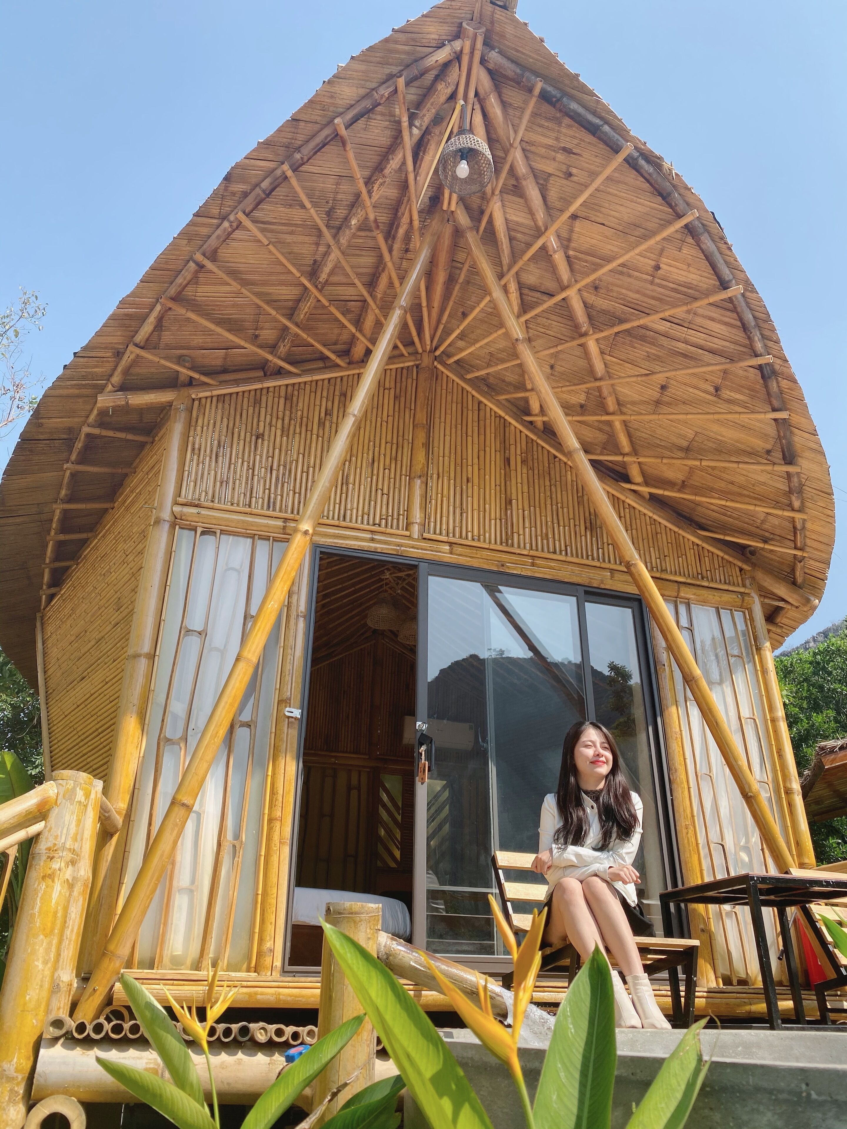 Una cabaña de bambú con puerta de vidrio y un pequeño espacio de estar al aire libre.