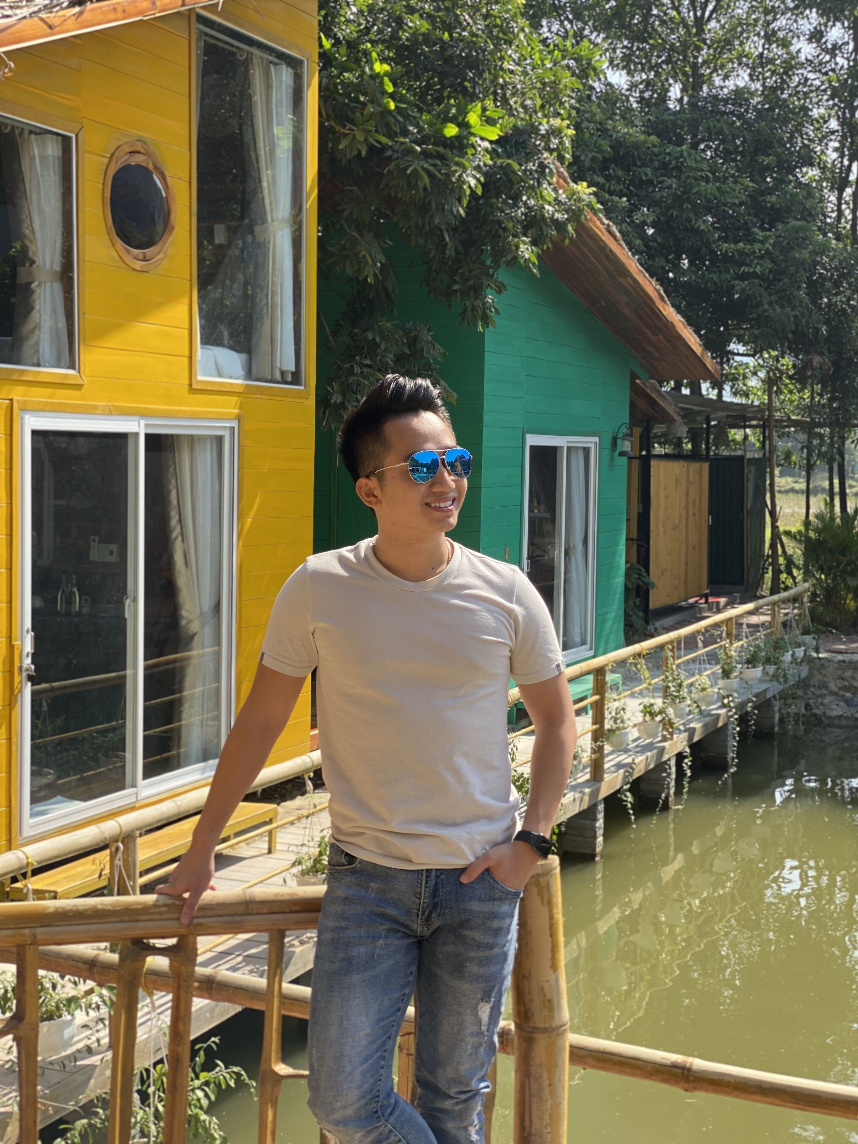 A person standing on a wooden bridge with a yellow building and a green building in the background.