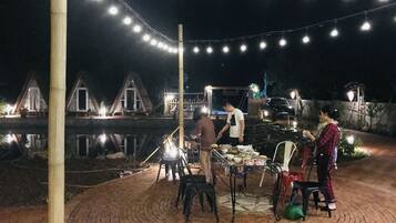 Een terras in de open lucht 's nachts, met lichtjes, een terrasvloer van baksteen en uitzicht op een waterpartij met gebouwen op de achtergrond.