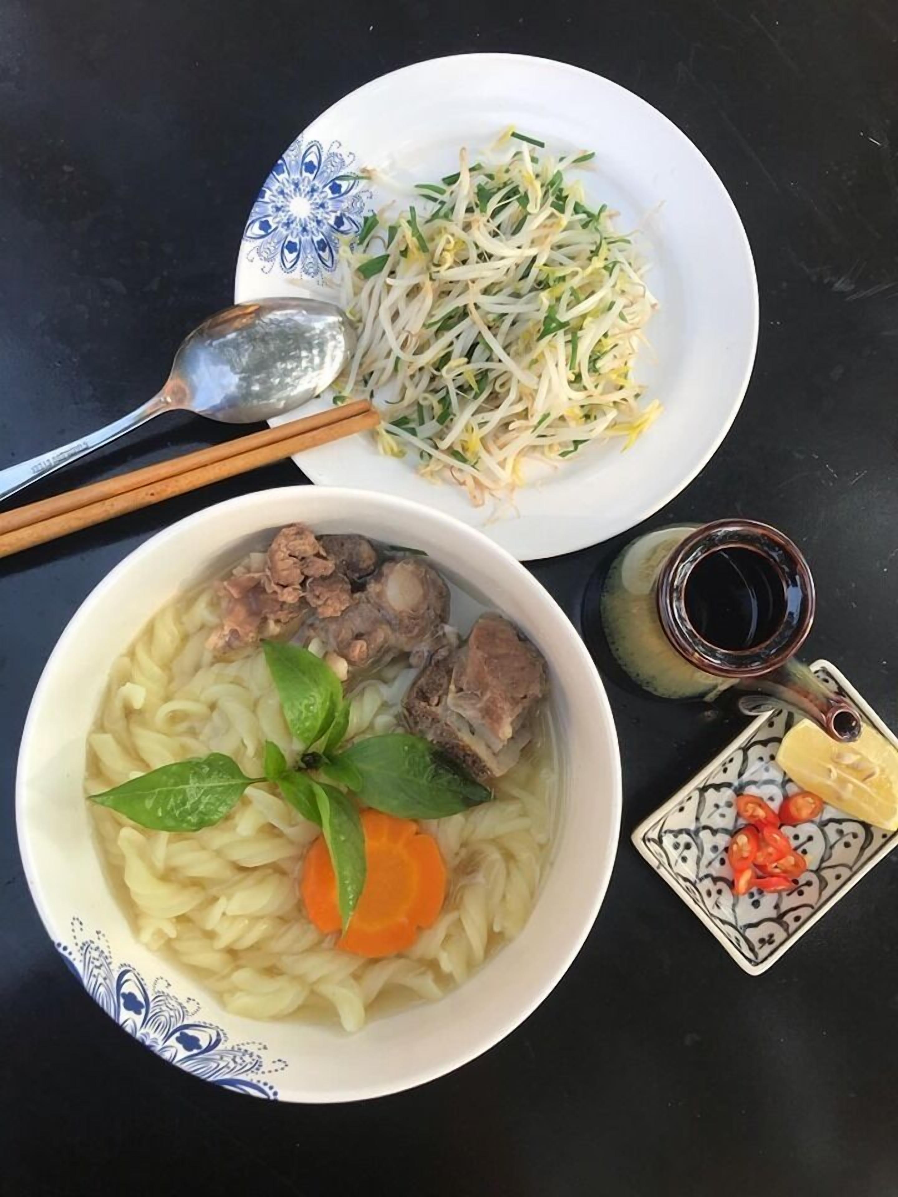 Dos tazones de comida, uno con fideos y carne, y otro con brotes de soja y vegetales, sobre una mesa negra.