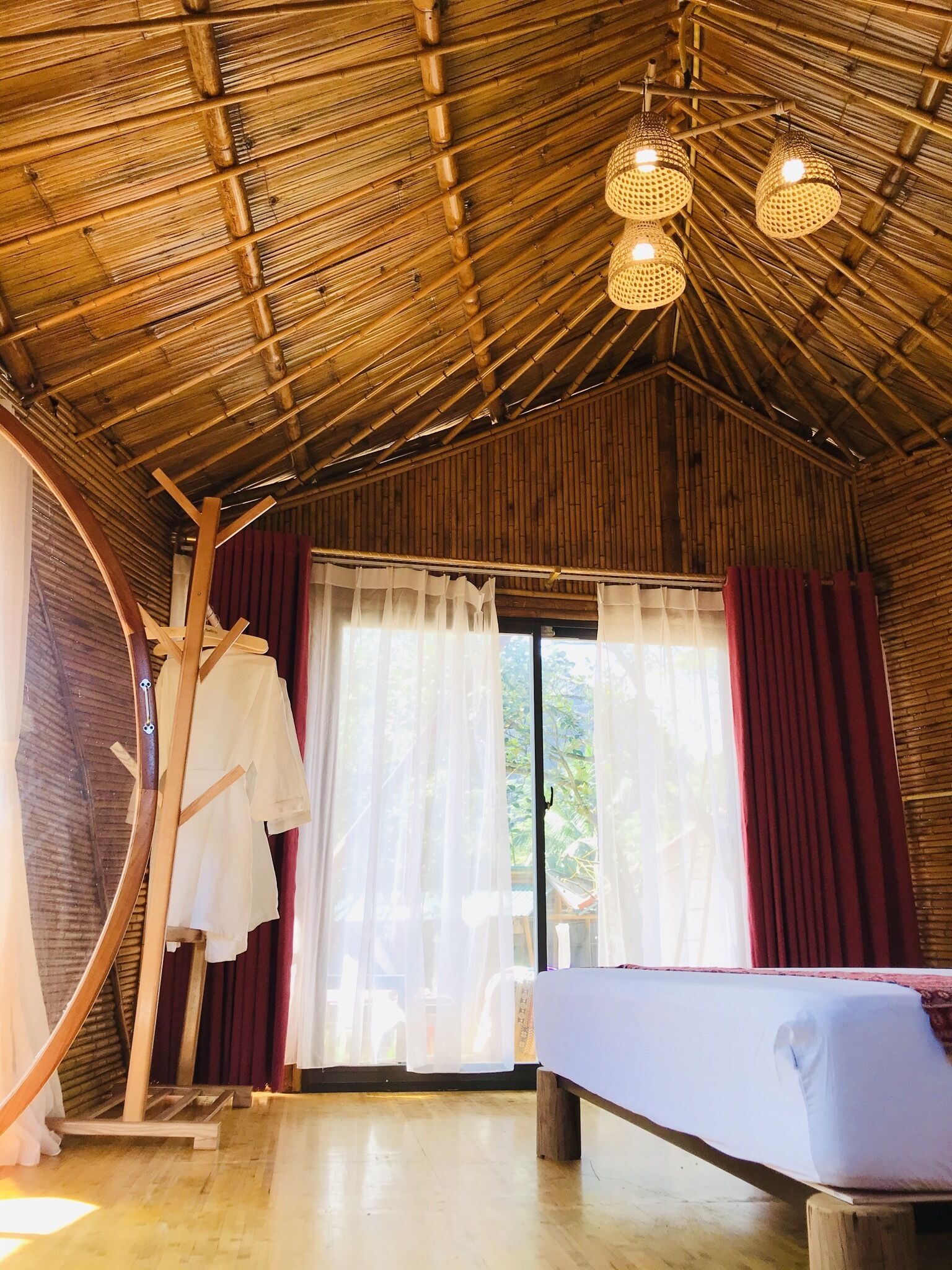 A room with a bamboo ceiling, a bed, a bench, and a clothing rack.