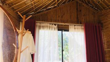 A room with a bamboo ceiling, a bed, a bench, and a clothing rack.