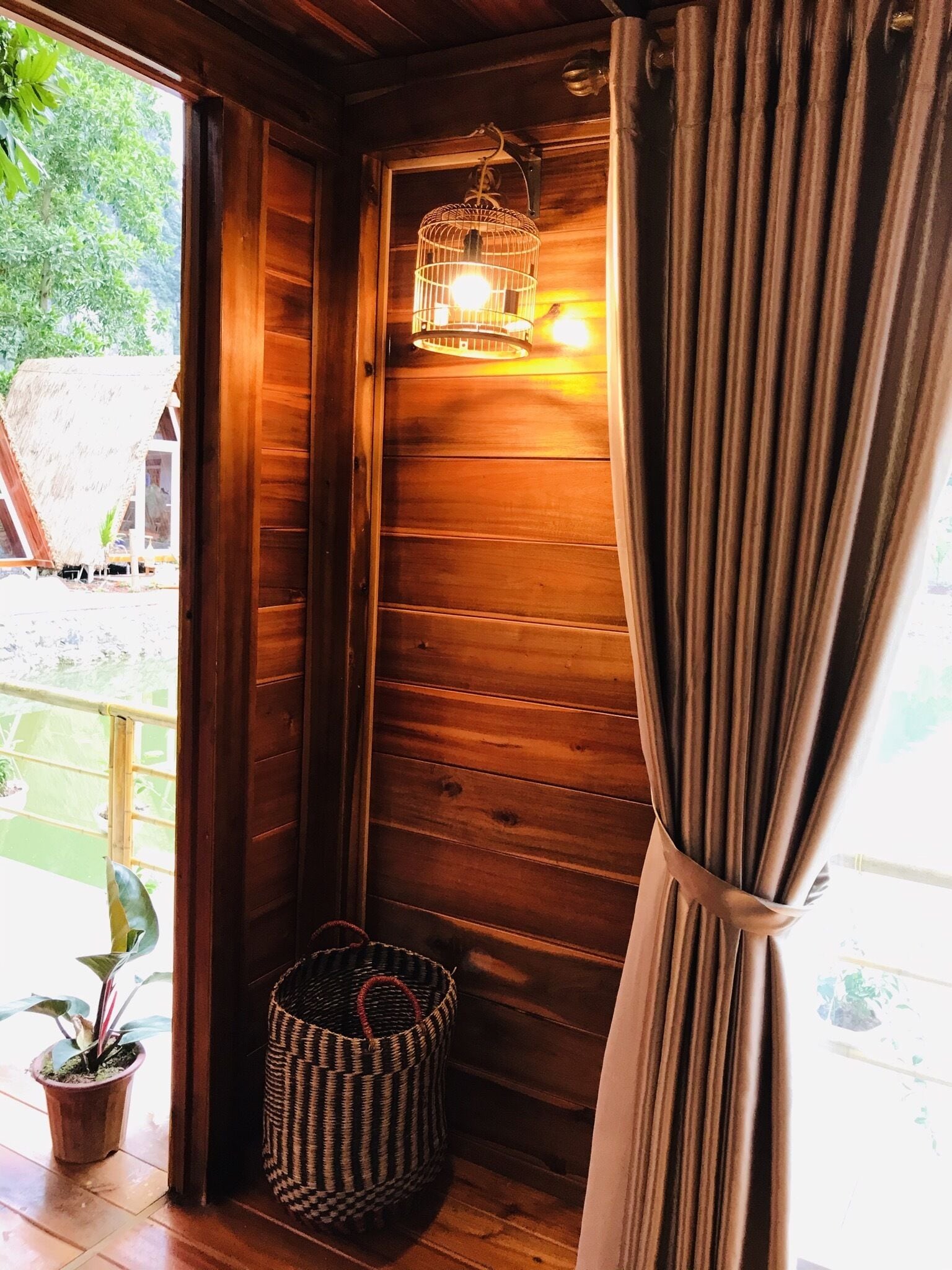 A wooden room with a curtain, a hanging light fixture, and a woven basket on the floor.