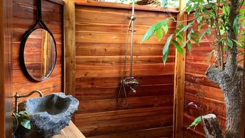 A wooden bathroom with a stone sink, a hanging mirror, and a shower.