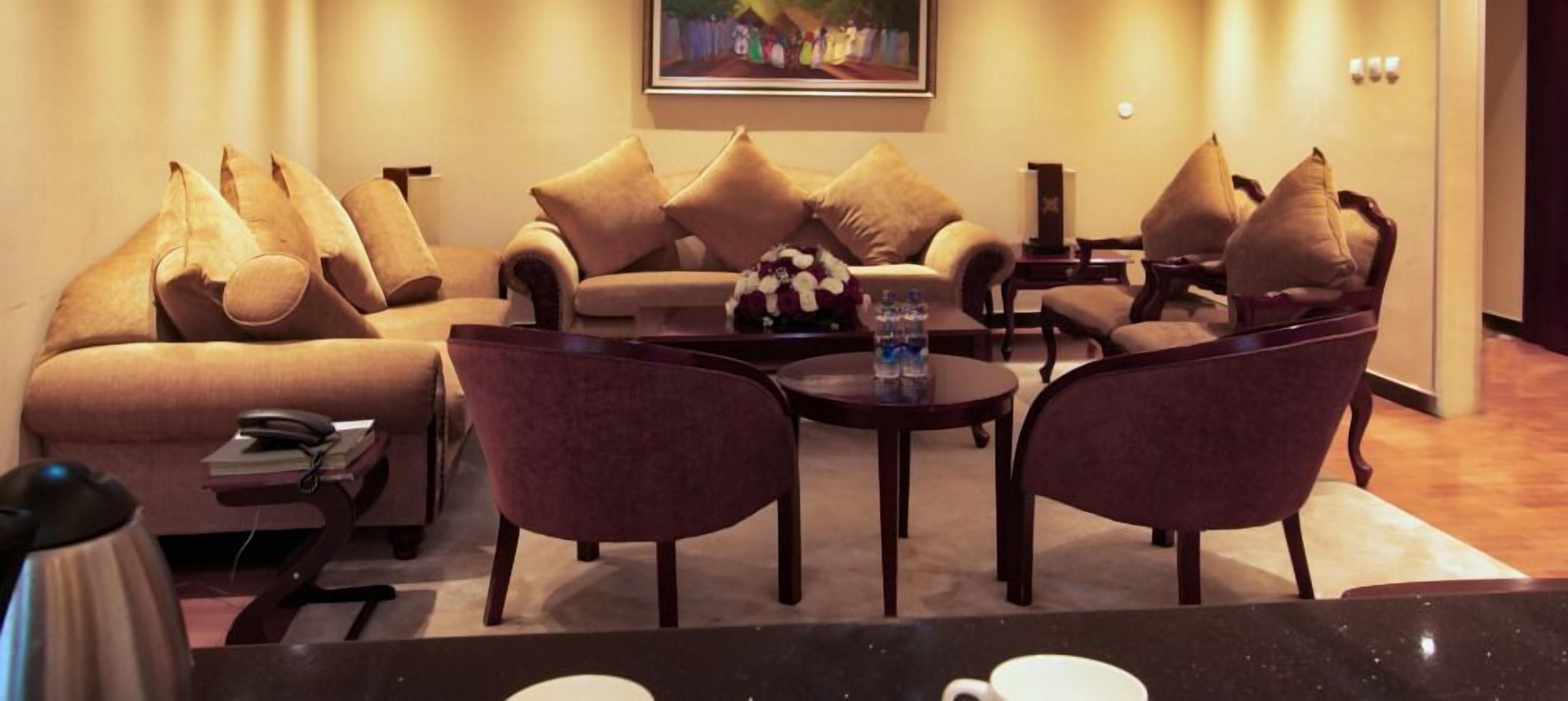 A cozy living room with a sofa set, two armchairs, a coffee table, and a small side table with a phone and books.