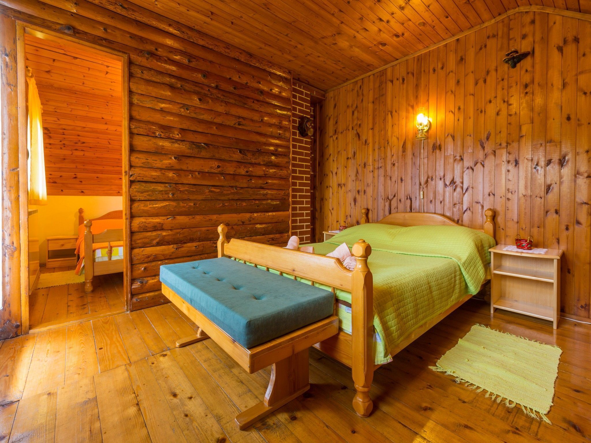 A wooden cabin bedroom with a bed, bench, nightstand, and wall-mounted lamp.