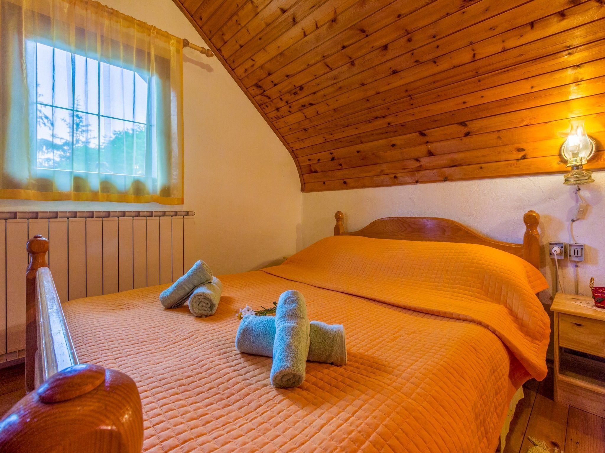 Ein gemütliches Schlafzimmer mit Holzbalkendecke, einem Bett mit orangefarbener Steppdecke und einem Fenster mit Vorhang.