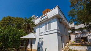 A modern two-story house with a balcony, a small patio with a table and chairs, and a garden area with a palm tree and a potted plant. - House Villa Vaho (Novi Vinodolski)