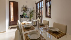 A dining area with a table set for four, including plates, glasses, and cutlery. There is a decorative wall piece above the table and a window with curtains to the right. - House Lara (Jadranovo)