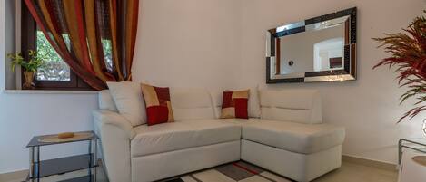 A modern living room with a white sectional sofa, a patterned rug, a small side table, and a large mirror on the wall.