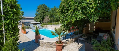 A pool area with stone flooring, potted plants, and outdoor furniture.