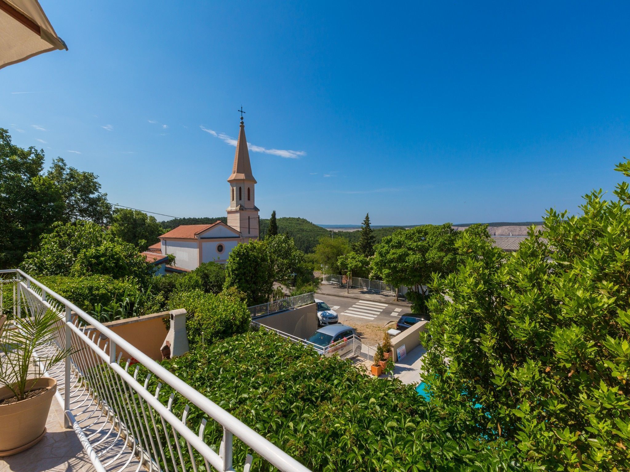 A view of a church with a tall spire, surrounded by lush greenery and a clear blue sky.
