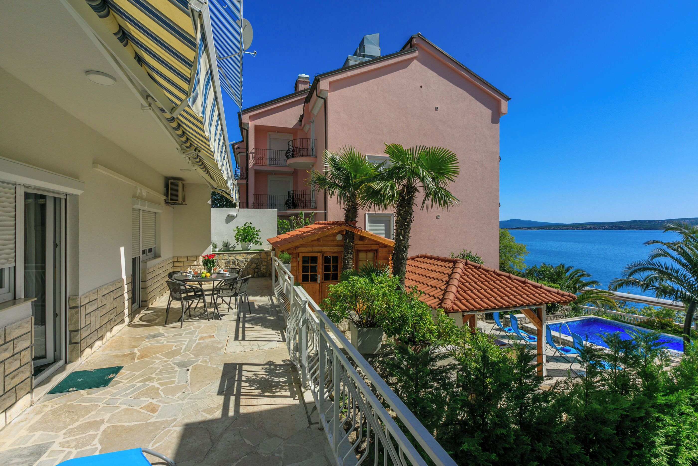 A balcony with a stone floor, a pool, and a view of the sea.