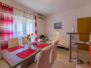 Ein zeitgemäßer Essbereich mit einem Holztisch, roten Untersetzern, weißen Stühlen und einem weißen Sofa.