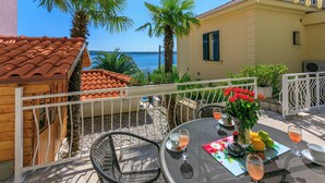 A terrace with a table set for two, overlooking a beach and a yellow building. - House Blanka (Dramalj)