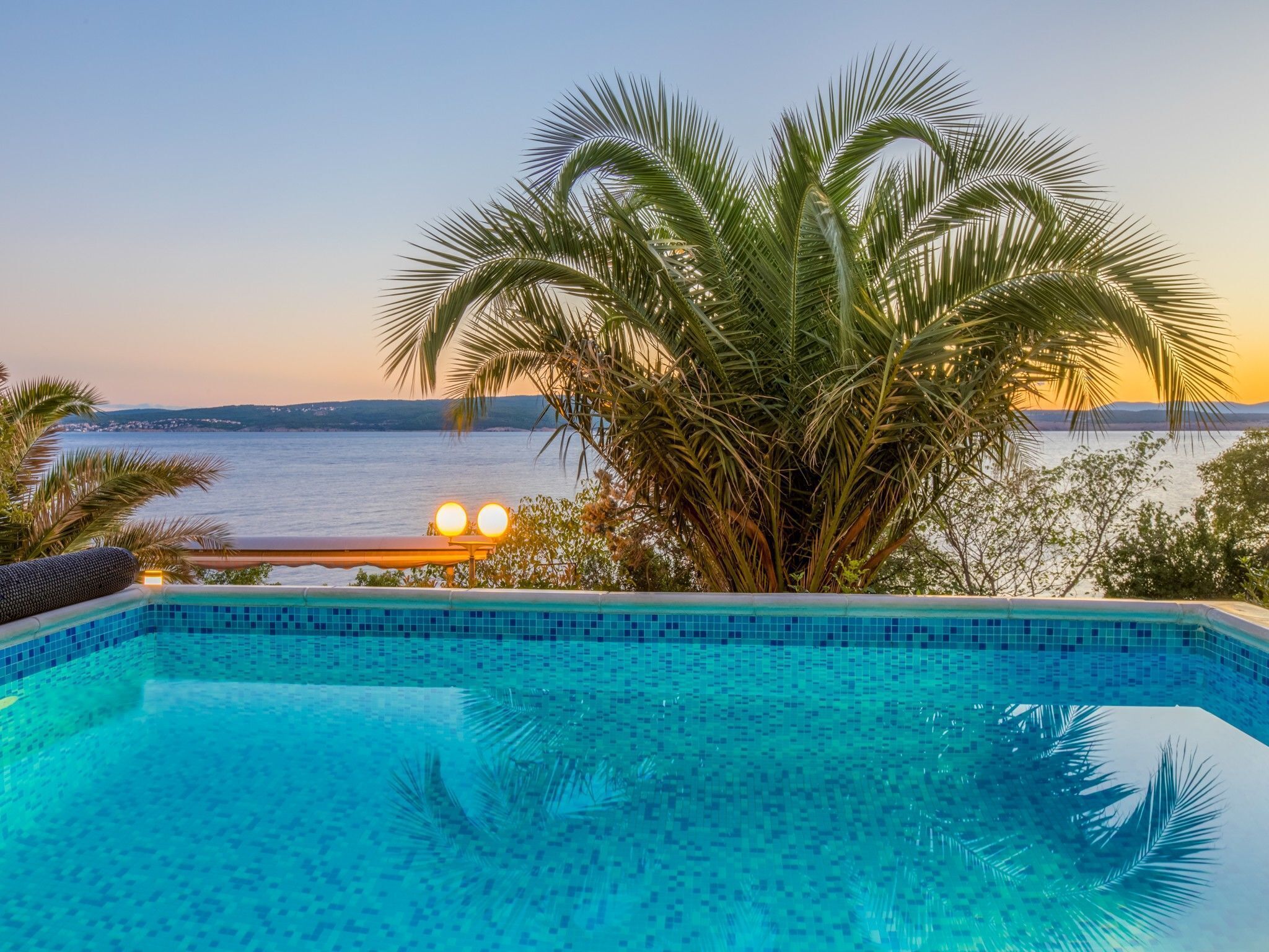 A swimming pool with a view of the sea at sunset.