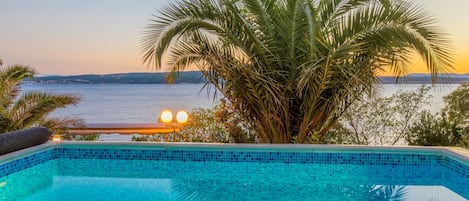 A swimming pool with a view of the sea at sunset.