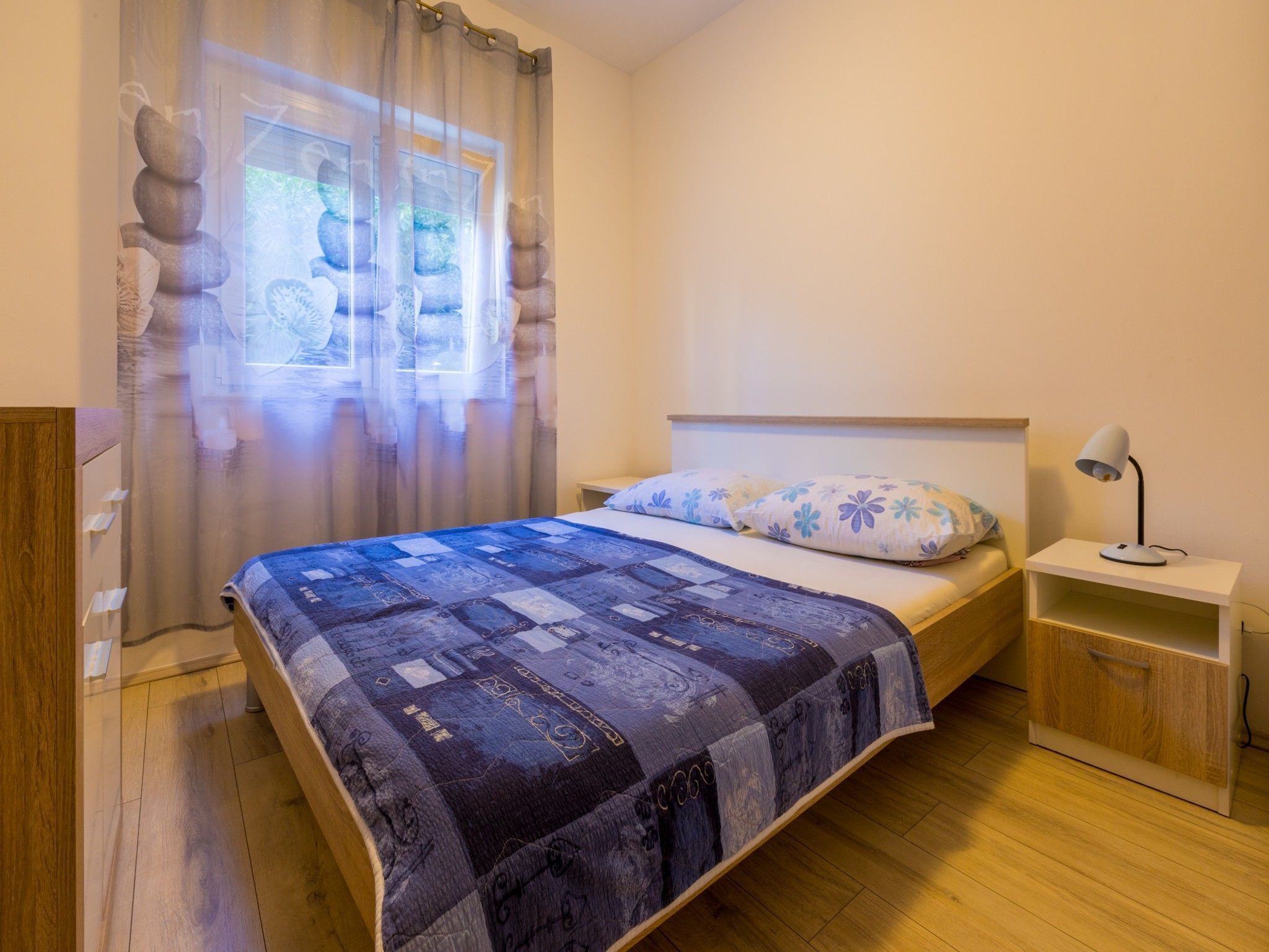 A bedroom with a bed, a nightstand, a lamp, and a window with curtains.