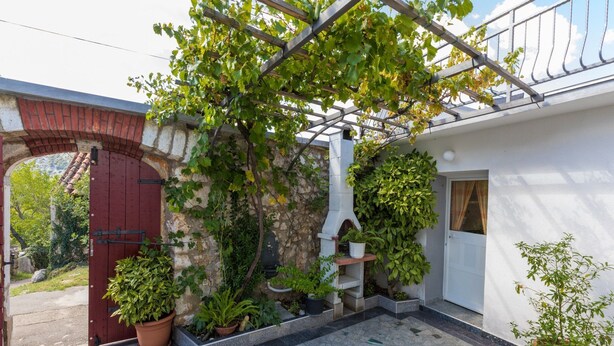 A courtyard with a stone wall, a red door, potted plants, and a white building with a balcony.