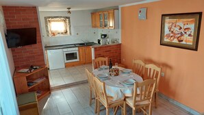 A compact kitchen with a dining area, featuring a brick wall, wooden cabinets, and a tiled floor.