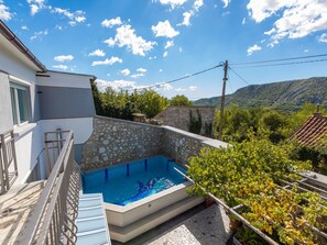 A private pool with stone walls, a balcony, and a view of a mountainous landscape. - House Delfin (Tribalj)