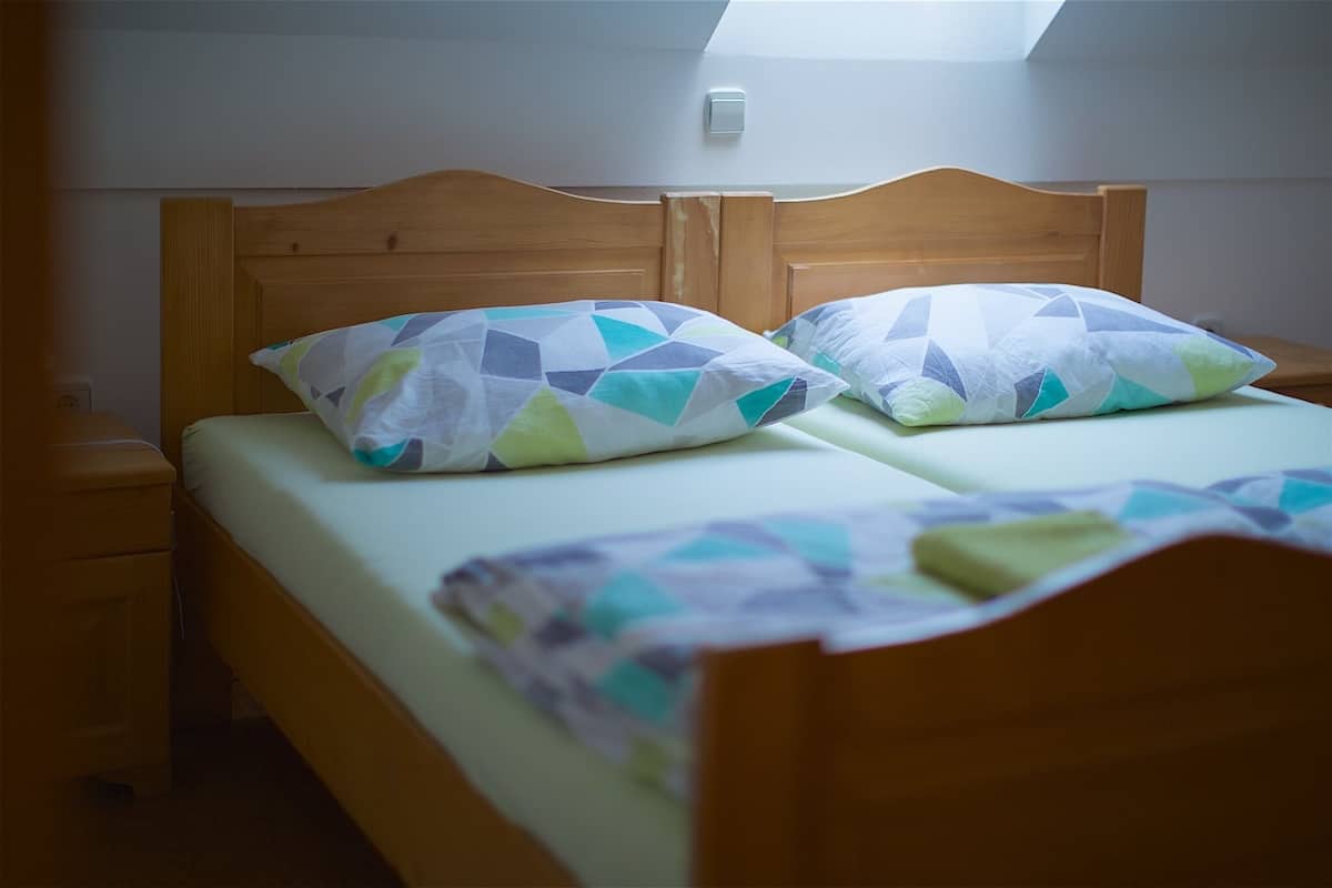 A double bed with a wooden headboard, two pillows with a geometric pattern, and a small bedside table.
