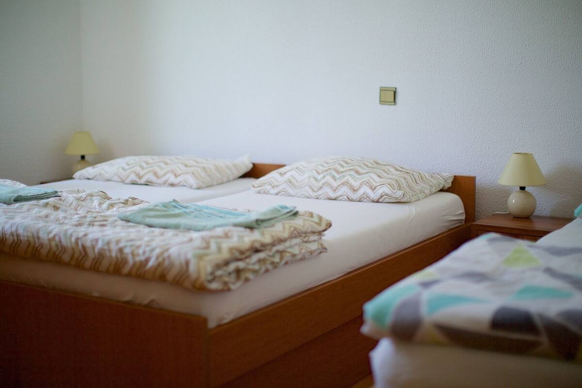 A hotel room with two beds, each with a wooden headboard, white bedding, and a small bedside table with a lamp.