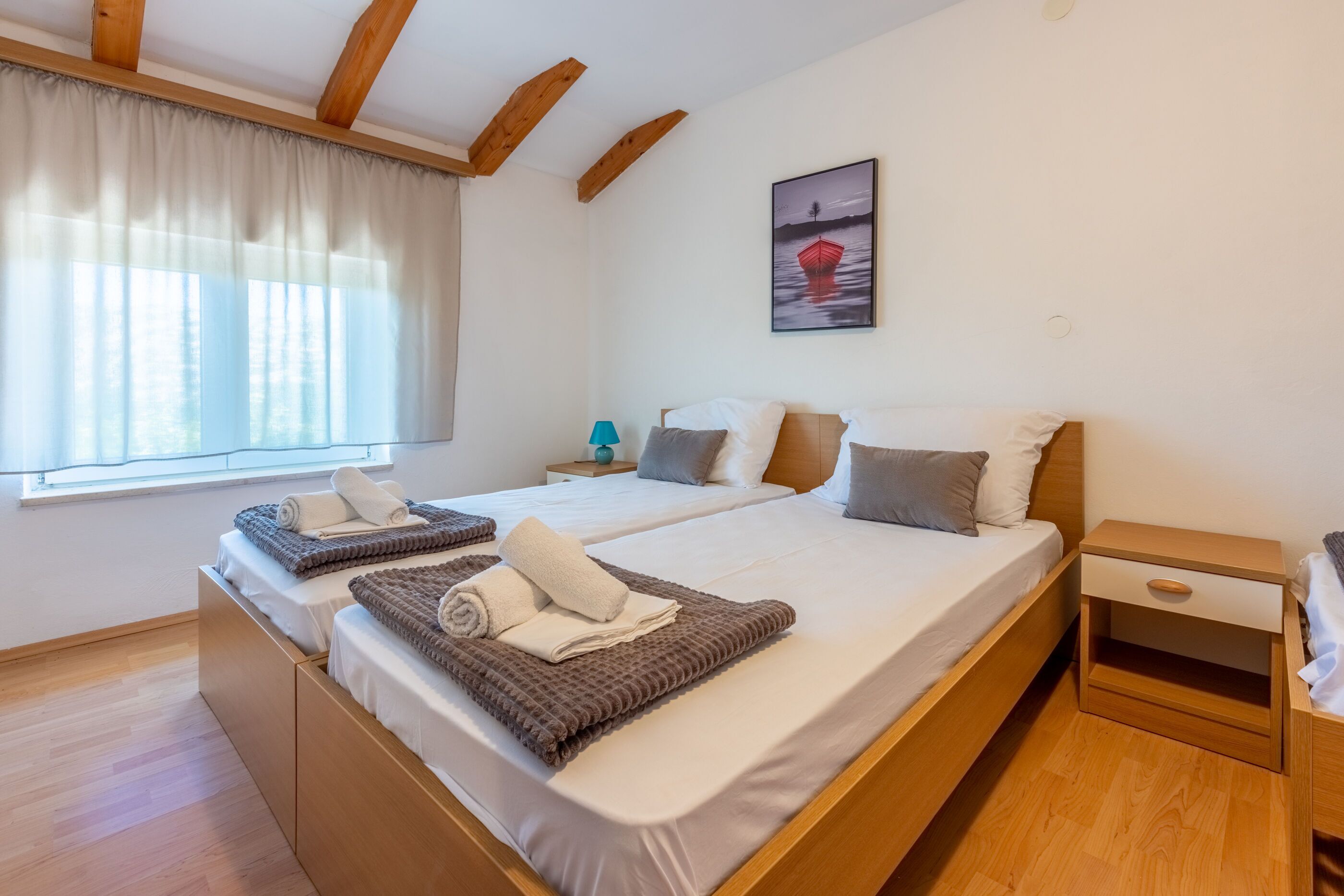 Ein Doppelbett mit hölzernem Kopfteil, ein Nachttisch mit Lampe und ein Fenster mit Vorhängen.