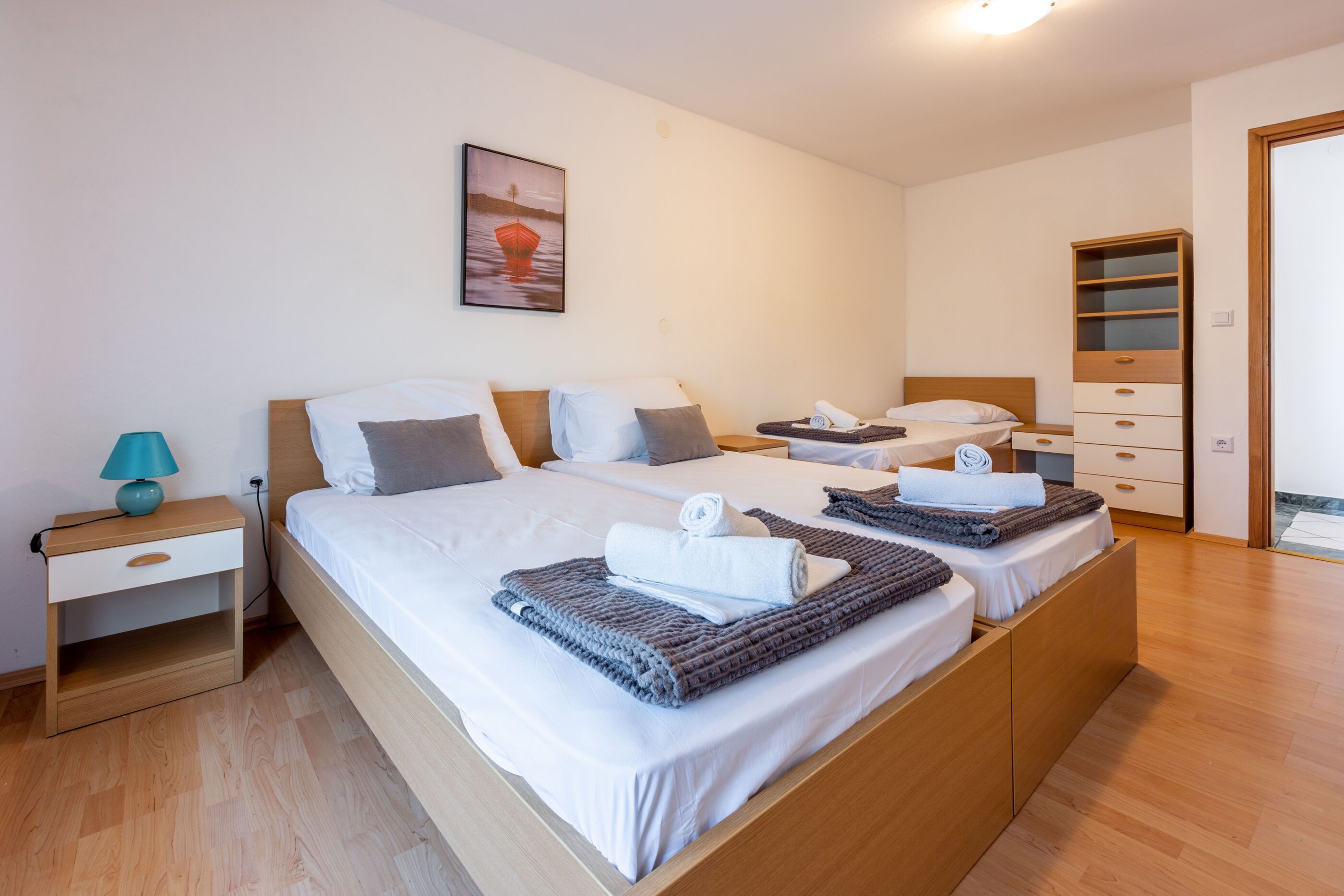 Ein Doppelbett mit Holz-Kopfteil, ein Nachttisch mit Lampe und ein Bild an der Wand.