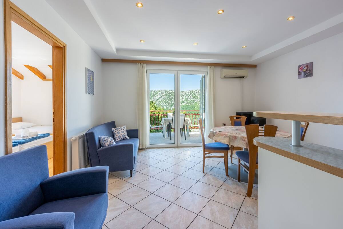A modern living room with a sofa, a dining table, and a balcony with a view of the mountains.