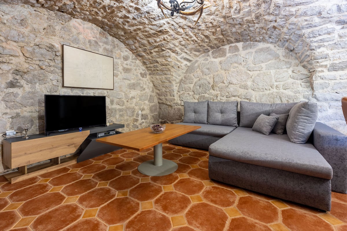 A cozy room with a stone wall, a flat-screen TV, a wooden coffee table, and a gray sofa.