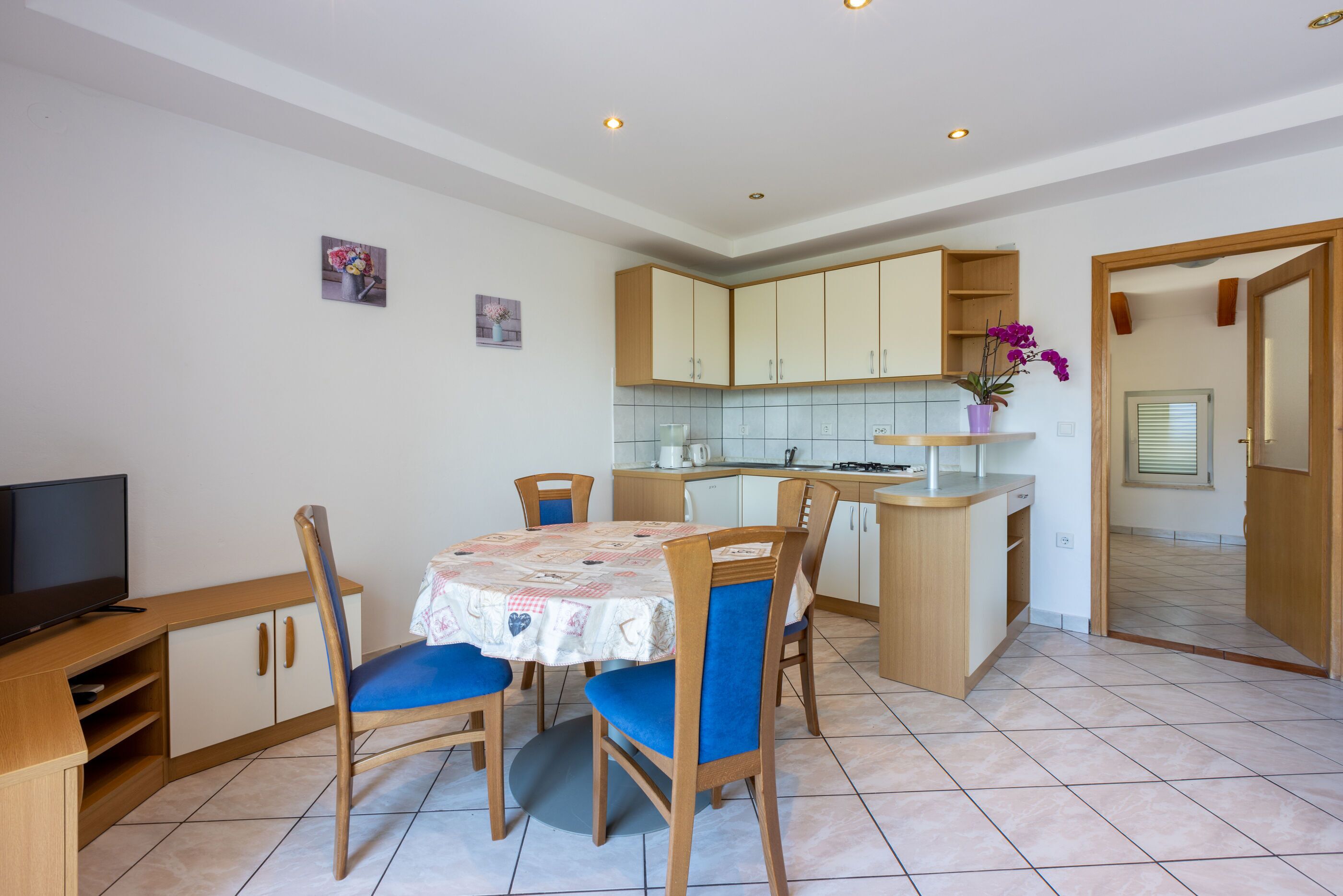 A compact kitchen with a dining area, wooden cabinets, a tiled backsplash, and a small island with a sink.