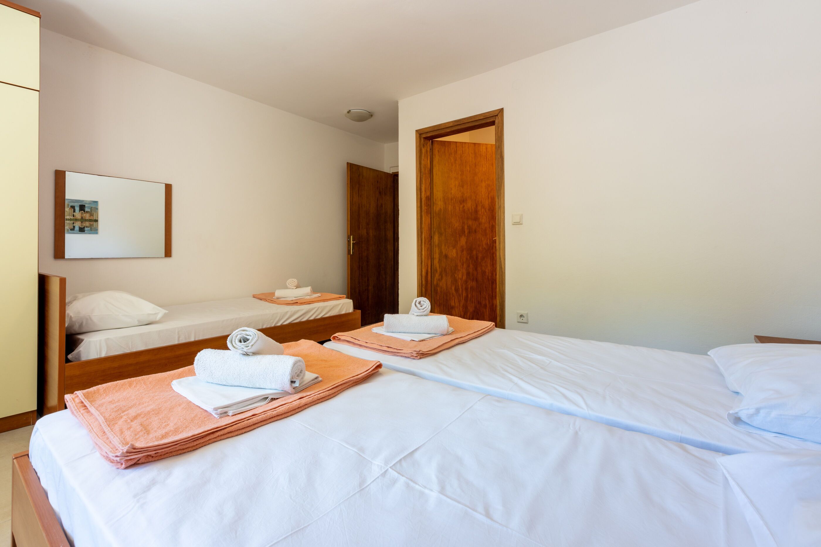 A hotel room with two beds, each with neatly folded towels, a wooden door, and a framed picture on the wall.