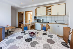 A compact kitchen with a microwave, coffee maker, and a sink. There is a dining table with chairs and a bowl of fruit.