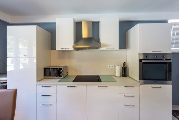 A modern kitchen with white cabinets, a built-in microwave, a gas stove, and a stainless steel range hood. - House Moderna 2 (Crikvenica)