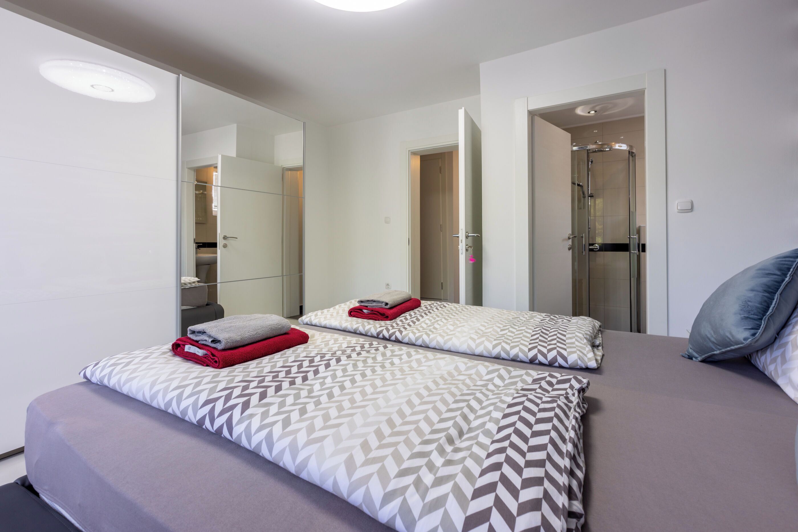 Ein modernes Hotelzimmer mit einem großen Bett, einem begehbaren Kleiderschrank und einem Badezimmer mit Duschkabine.